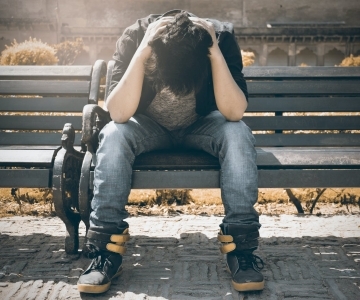 man in black shirt and gray denim pants sitting on gray padded bench